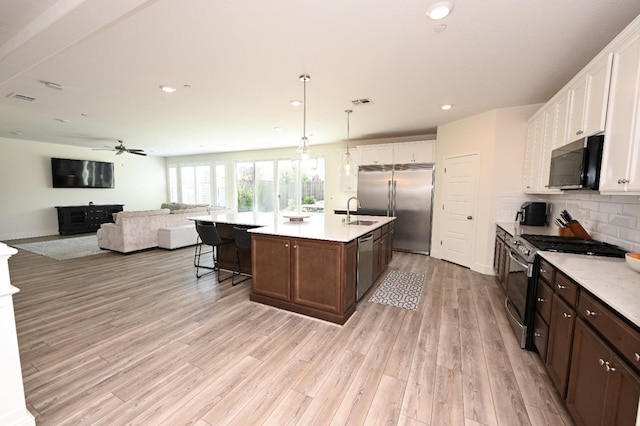 kitchen featuring a sink, tasteful backsplash, stainless steel appliances, light wood-style floors, and light countertops