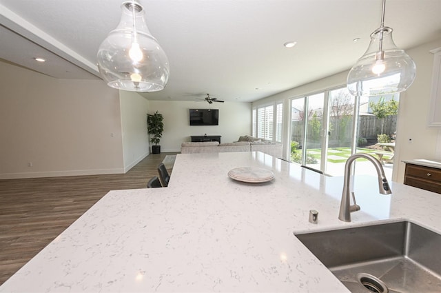 kitchen with pendant lighting, a sink, light stone counters, wood finished floors, and open floor plan