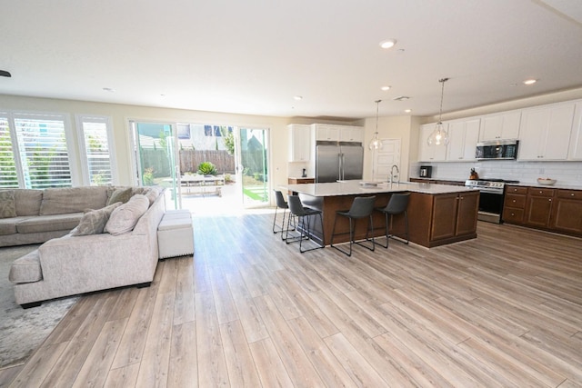 kitchen featuring light wood-style flooring, stainless steel appliances, light countertops, white cabinetry, and open floor plan