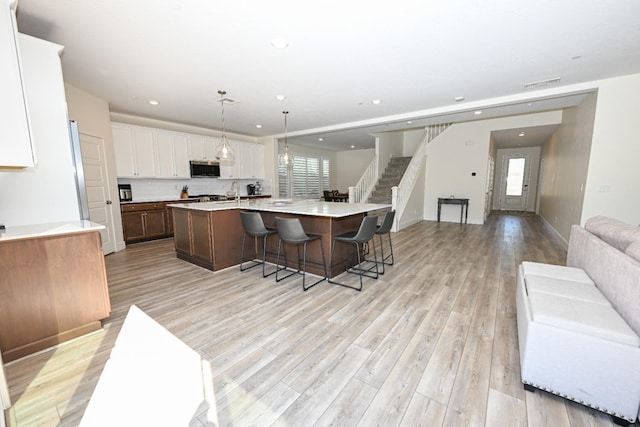 kitchen featuring light wood finished floors, a large island, white cabinetry, stainless steel microwave, and open floor plan