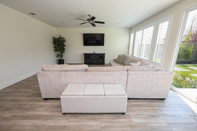 living room featuring a ceiling fan, visible vents, light wood-type flooring, and baseboards