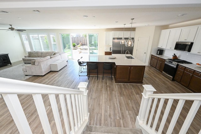 kitchen featuring a sink, tasteful backsplash, wood finished floors, stainless steel appliances, and dark brown cabinets