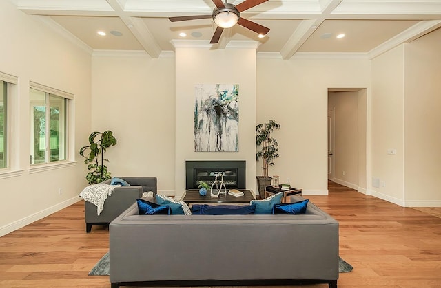 living area with coffered ceiling, a glass covered fireplace, beam ceiling, crown molding, and light wood finished floors
