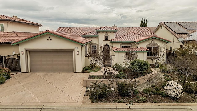 mediterranean / spanish-style house featuring concrete driveway, a tile roof, an attached garage, stucco siding, and fence