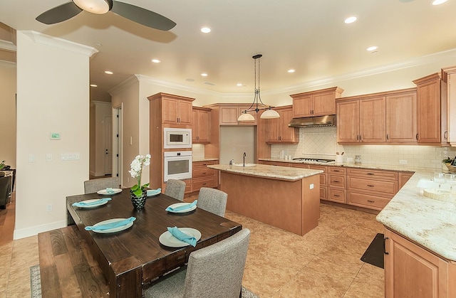 kitchen with ornamental molding, under cabinet range hood, light stone counters, tasteful backsplash, and white appliances