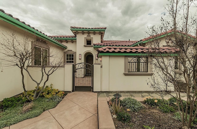 exterior space with stucco siding, fence, a tile roof, and a gate