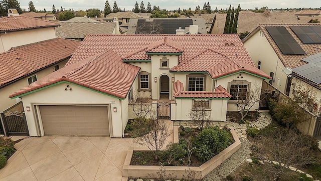 mediterranean / spanish-style home featuring a fenced front yard, a tiled roof, concrete driveway, an attached garage, and a gate