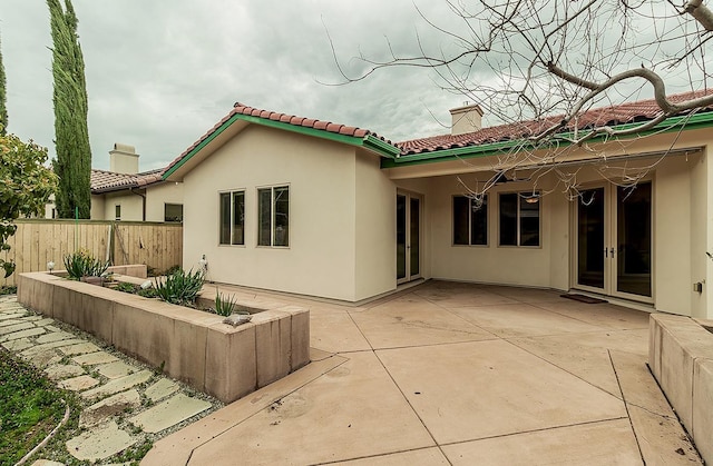 back of house with stucco siding, a patio, fence, french doors, and a chimney