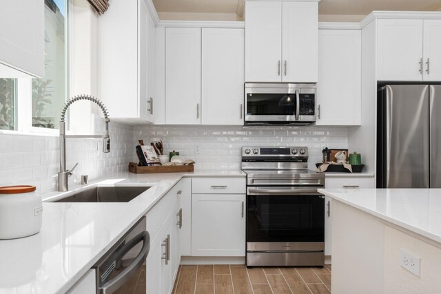 kitchen with tasteful backsplash, wood finish floors, white cabinets, stainless steel appliances, and a sink