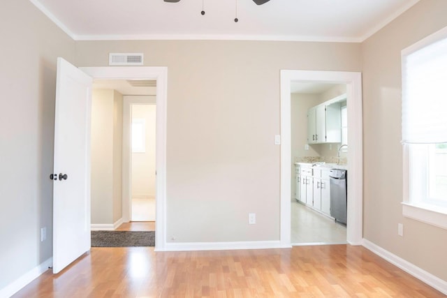 empty room with light wood finished floors, visible vents, baseboards, and ornamental molding