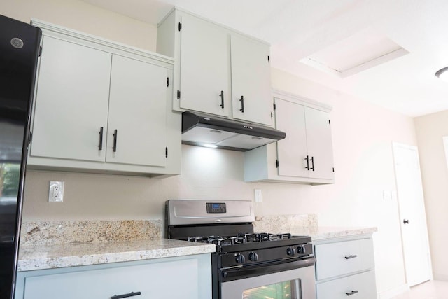 kitchen featuring under cabinet range hood, stainless steel gas stove, refrigerator, and white cabinetry