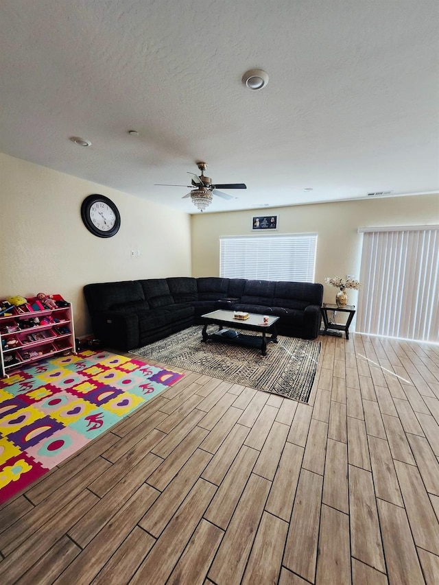 living room featuring a textured ceiling, a ceiling fan, visible vents, and wood tiled floor