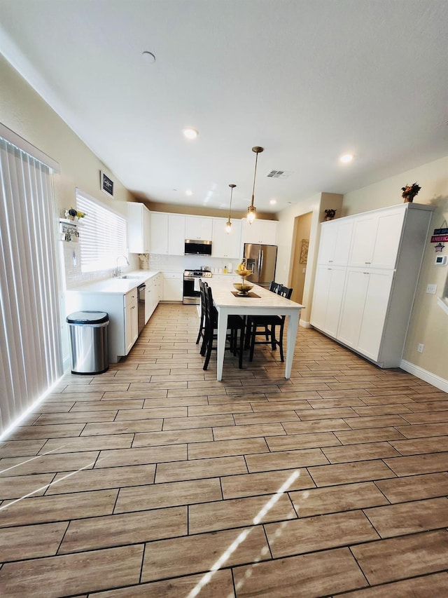 kitchen featuring pendant lighting, appliances with stainless steel finishes, white cabinets, light countertops, and wood tiled floor