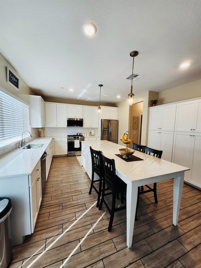 kitchen featuring wood finish floors, stainless steel appliances, visible vents, and white cabinetry