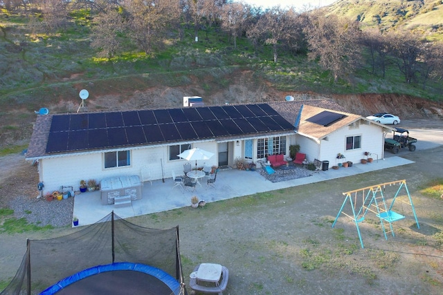 back of property featuring outdoor dining area, a trampoline, solar panels, and a patio area