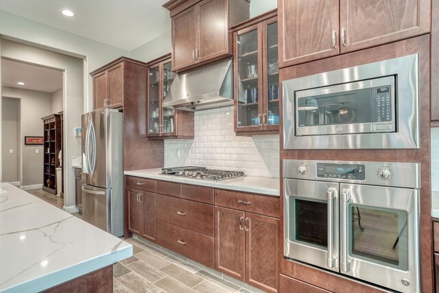 301 Pinnacle Dr W, Madera, CA 93636 - kitchen with stainless steel appliances, under cabinet range hood, decorative backsplash, light stone countertops, and glass insert cabinets