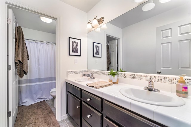 full bath featuring double vanity, decorative backsplash, toilet, and a sink