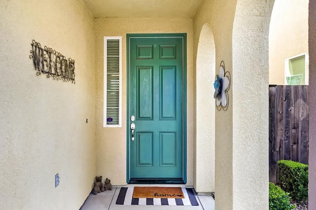 view of exterior entry with stucco siding and fence