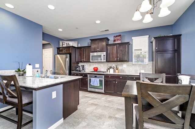 kitchen with a kitchen bar, arched walkways, dark brown cabinetry, appliances with stainless steel finishes, and decorative backsplash