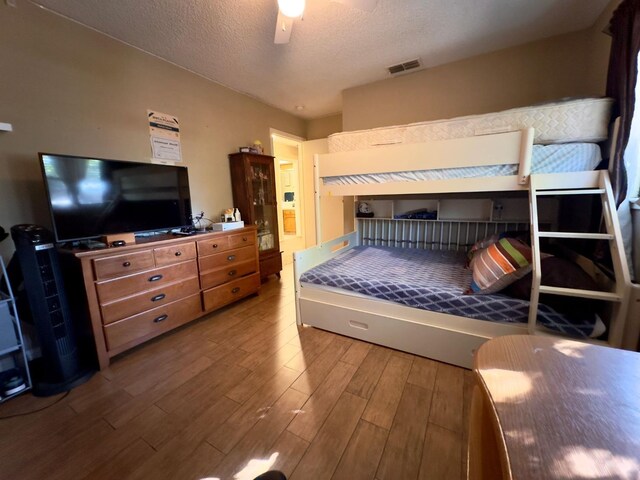 bedroom featuring visible vents, a textured ceiling, a ceiling fan, and wood finished floors