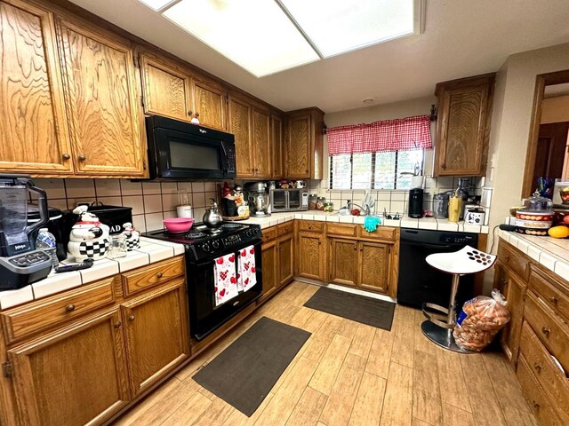 kitchen featuring tasteful backsplash, tile counters, light wood-style flooring, black appliances, and a sink