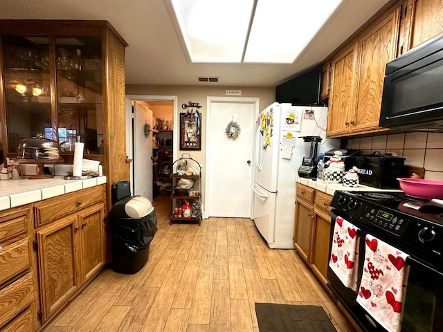 kitchen with tile countertops, light wood-style floors, black appliances, and brown cabinetry