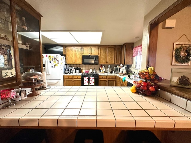 kitchen featuring tile countertops, a peninsula, and black appliances