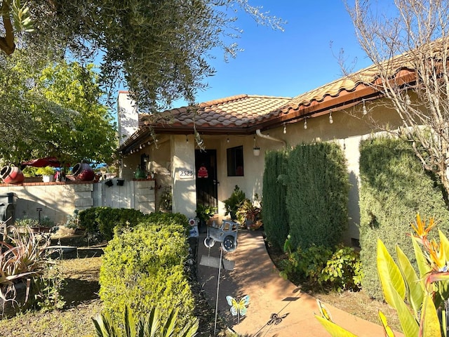 view of front of property with stucco siding, a tiled roof, a chimney, and fence