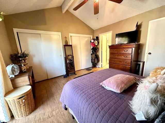 bedroom featuring multiple closets, lofted ceiling with beams, a textured ceiling, a ceiling fan, and wood-type flooring