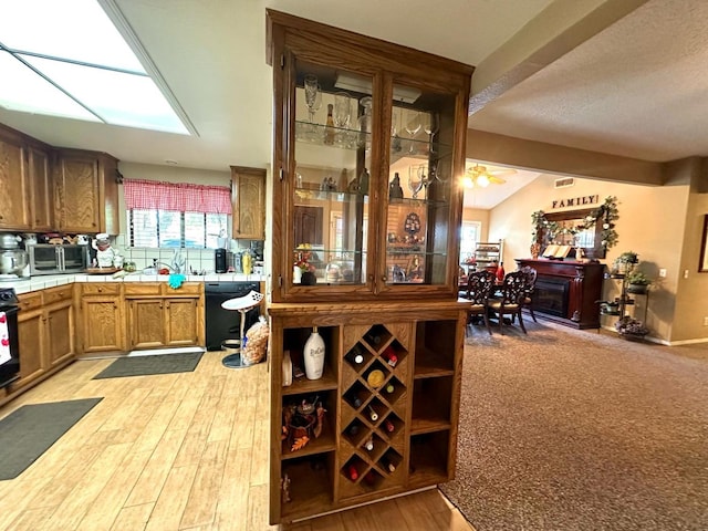 bar with light wood finished floors, a fireplace, vaulted ceiling, black dishwasher, and stainless steel microwave