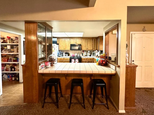 kitchen with tile countertops, a peninsula, black appliances, and a breakfast bar area