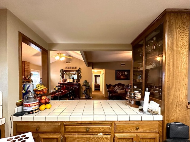 kitchen with brown cabinetry, open floor plan, lofted ceiling, and tile counters