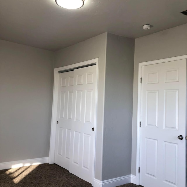 unfurnished bedroom featuring visible vents, baseboards, a closet, and dark carpet