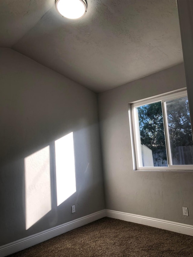 spare room featuring dark carpet, baseboards, and lofted ceiling