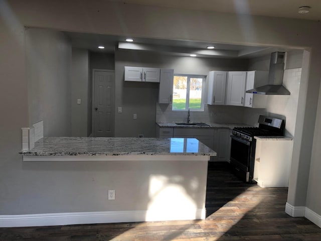 kitchen with a sink, range with gas stovetop, a peninsula, wall chimney range hood, and light stone countertops