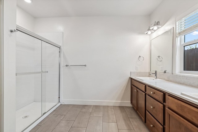 bathroom featuring a sink, baseboards, a stall shower, and double vanity