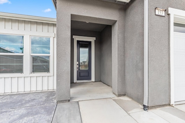 view of exterior entry featuring stucco siding, board and batten siding, and a garage