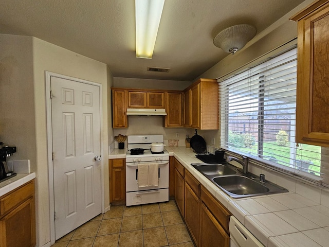 kitchen with visible vents, a sink, under cabinet range hood, tile countertops, and white appliances