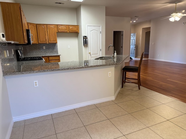 kitchen with dark stone counters, range with gas stovetop, light tile patterned flooring, brown cabinetry, and a sink