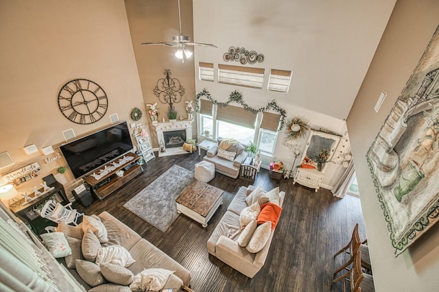 living room with ceiling fan, wood finished floors, a glass covered fireplace, and a towering ceiling