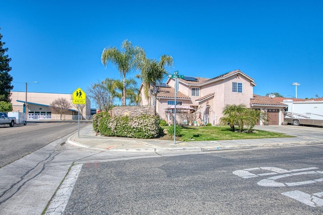 view of front of property with a tiled roof, an attached garage, roof mounted solar panels, and stucco siding