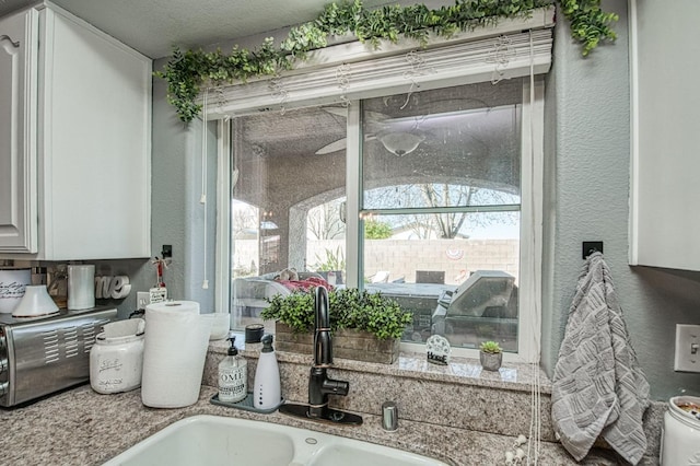 interior details featuring a toaster, white cabinets, a textured wall, and a sink