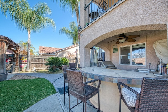 view of patio with fence, area for grilling, ceiling fan, a sink, and a grill