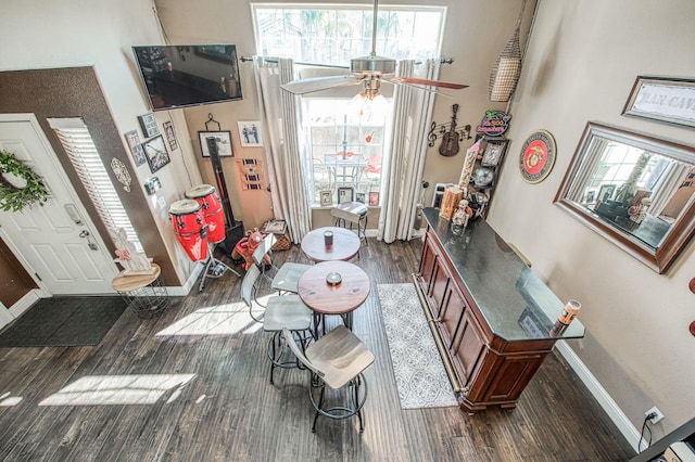 living room with ceiling fan, baseboards, a high ceiling, and dark wood-style floors