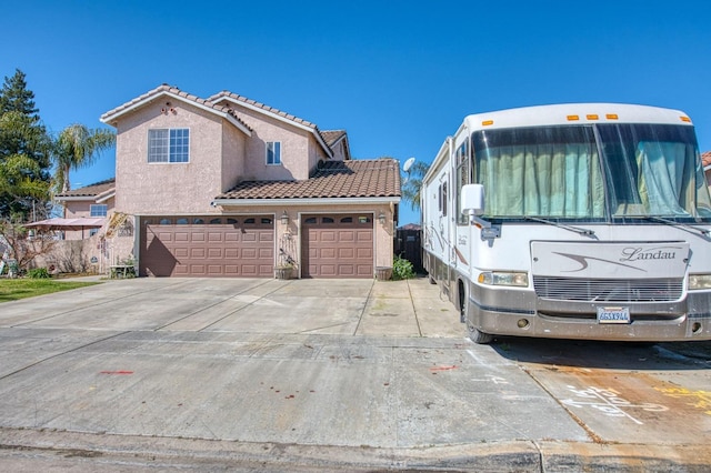 view of front facade with stucco siding, a tiled roof, driveway, and a garage