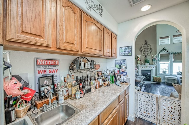 kitchen featuring arched walkways, dark wood-style flooring, a sink, light countertops, and a glass covered fireplace