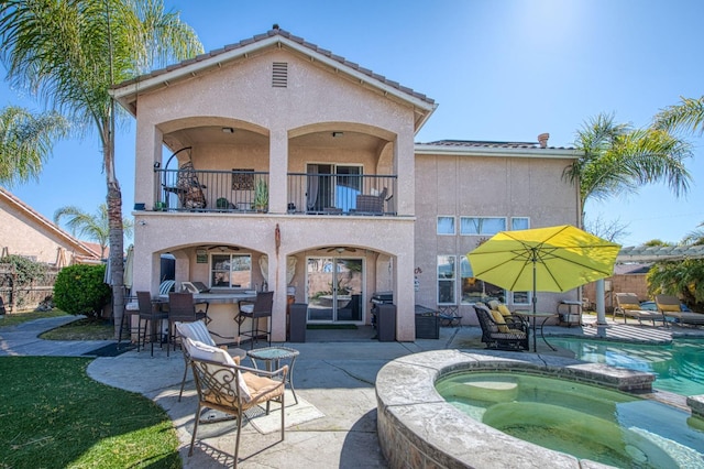 rear view of property featuring stucco siding, a patio, a balcony, and outdoor dry bar