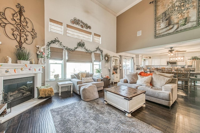 living room featuring visible vents, a glass covered fireplace, dark wood-style floors, crown molding, and a towering ceiling