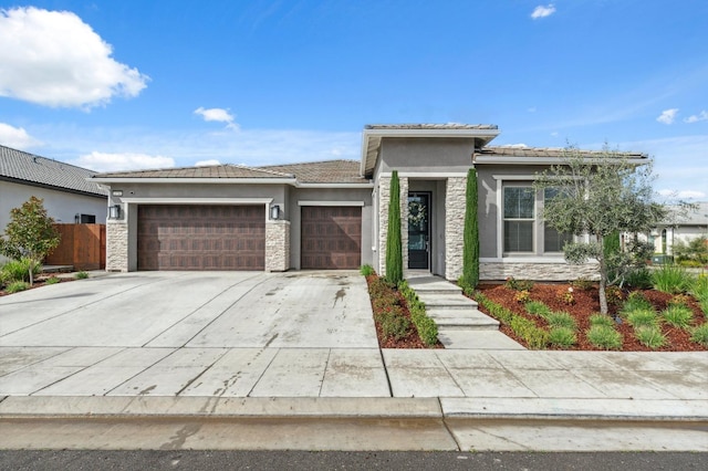 prairie-style home featuring fence, driveway, an attached garage, stucco siding, and stone siding