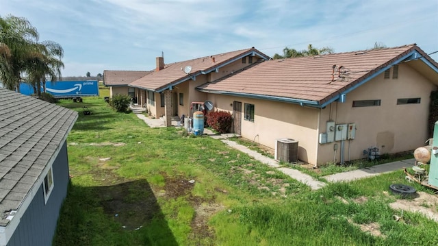 back of house with central air condition unit, a yard, and stucco siding